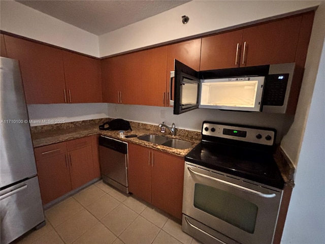 kitchen with light tile patterned flooring, stainless steel appliances, sink, and dark stone counters