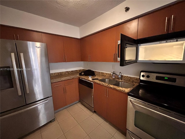 kitchen featuring appliances with stainless steel finishes, sink, dark stone counters, light tile patterned floors, and a textured ceiling