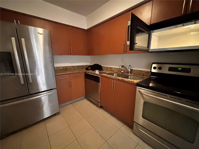 kitchen featuring appliances with stainless steel finishes, sink, light tile patterned floors, and dark stone counters