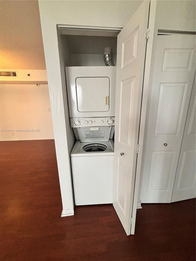 laundry area with dark hardwood / wood-style floors and stacked washing maching and dryer