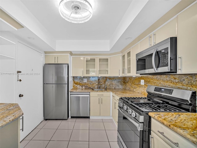 kitchen with backsplash, cream cabinets, sink, appliances with stainless steel finishes, and light tile patterned flooring