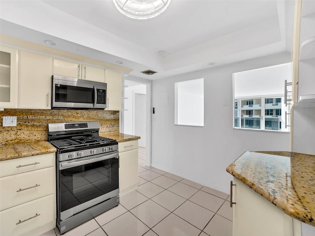 kitchen with cream cabinets, stainless steel appliances, light stone counters, and tasteful backsplash