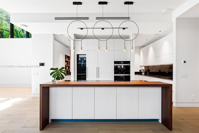 kitchen featuring white cabinets, stainless steel double oven, hanging light fixtures, and light hardwood / wood-style flooring