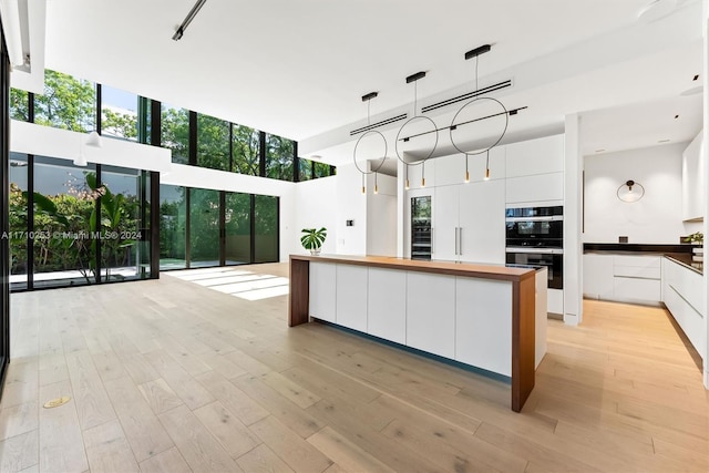 kitchen with decorative light fixtures, light hardwood / wood-style flooring, white cabinetry, and black double oven