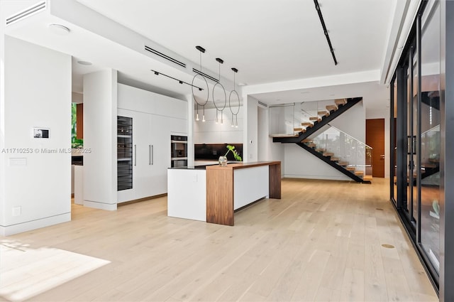 kitchen with decorative light fixtures, light wood-type flooring, modern cabinets, and white cabinetry