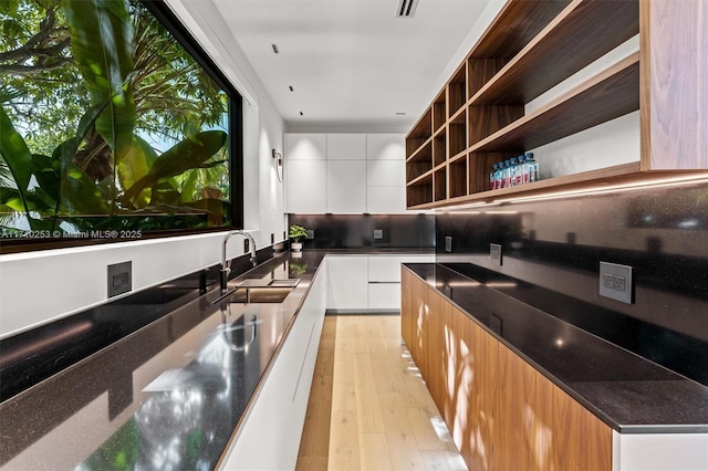 kitchen with a sink, light wood-type flooring, white cabinets, modern cabinets, and open shelves