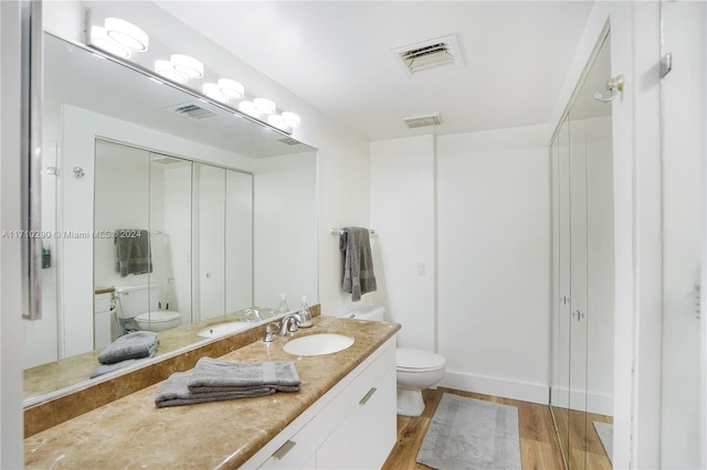 bathroom with walk in shower, hardwood / wood-style floors, vanity, and toilet