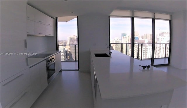 kitchen with white cabinetry, stainless steel oven, sink, a wall of windows, and black electric stovetop