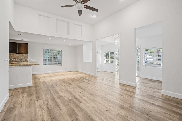 unfurnished living room featuring ceiling fan with notable chandelier and light hardwood / wood-style flooring