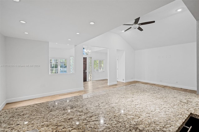 unfurnished living room featuring ceiling fan with notable chandelier, light hardwood / wood-style floors, and lofted ceiling