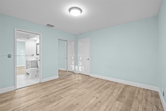 unfurnished bedroom featuring light wood-type flooring, ensuite bath, and a closet