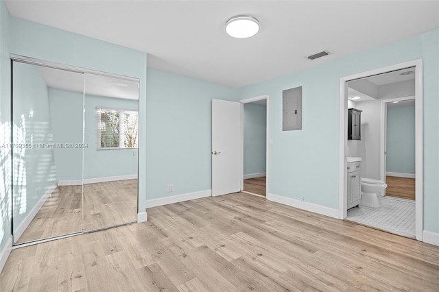 unfurnished bedroom featuring electric panel, ensuite bath, light hardwood / wood-style flooring, and a closet