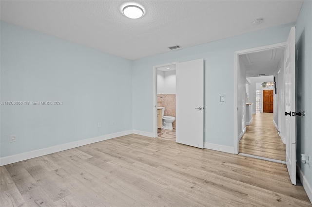 unfurnished bedroom featuring ensuite bath, a textured ceiling, and light wood-type flooring