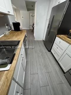 kitchen featuring wood counters, stainless steel fridge, and white cabinetry