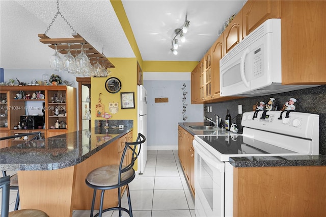 kitchen with white appliances, sink, light tile patterned floors, a textured ceiling, and a kitchen bar