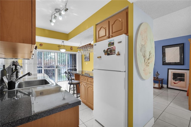 kitchen with sink, white fridge, light tile patterned flooring, and a textured ceiling