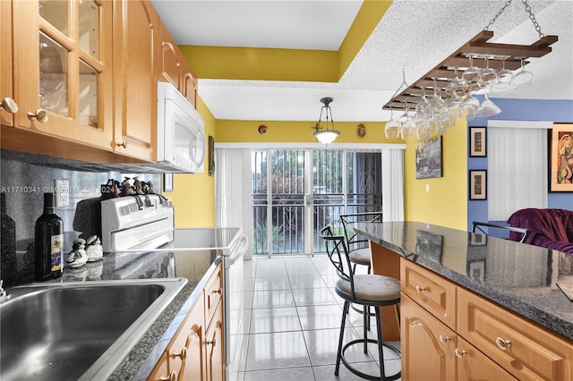 kitchen featuring a kitchen breakfast bar, pendant lighting, a textured ceiling, white appliances, and light tile patterned flooring