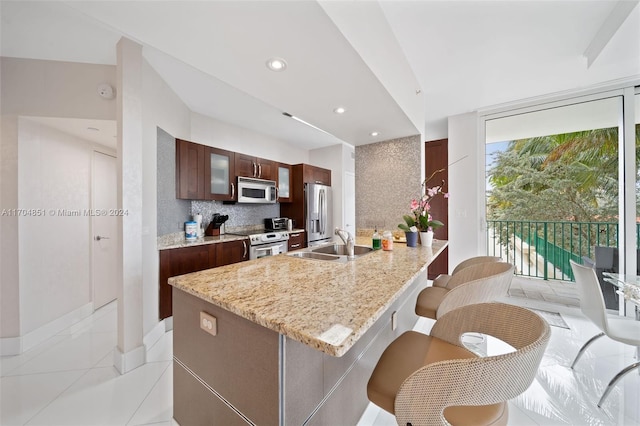 kitchen with a kitchen bar, light stone counters, stainless steel appliances, sink, and light tile patterned floors