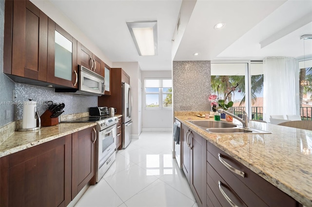 kitchen with sink, stainless steel appliances, light stone counters, backsplash, and dark brown cabinets