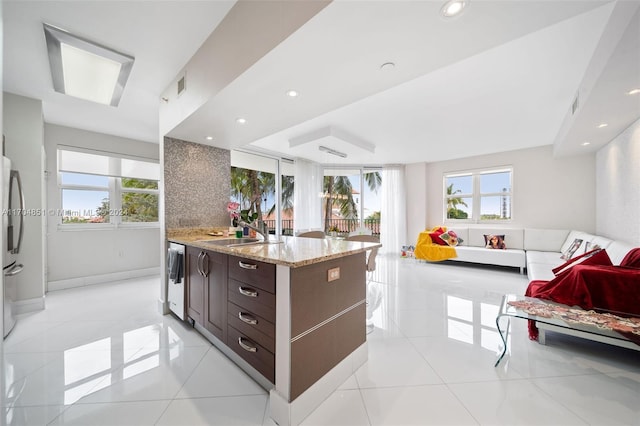 kitchen with light stone countertops, sink, dark brown cabinets, light tile patterned floors, and appliances with stainless steel finishes