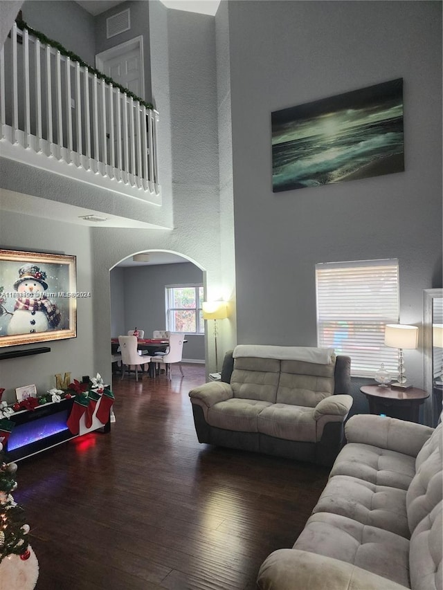 living room with a towering ceiling and dark wood-type flooring