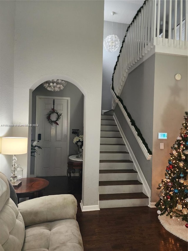 staircase with hardwood / wood-style floors, a towering ceiling, and an inviting chandelier