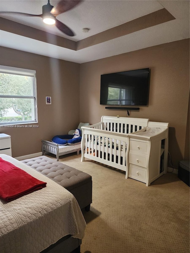 bedroom featuring a raised ceiling, ceiling fan, and light colored carpet