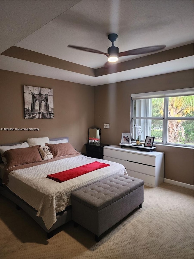 bedroom with light carpet, a tray ceiling, and ceiling fan