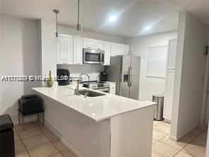 kitchen with white cabinetry, hanging light fixtures, kitchen peninsula, a kitchen bar, and appliances with stainless steel finishes