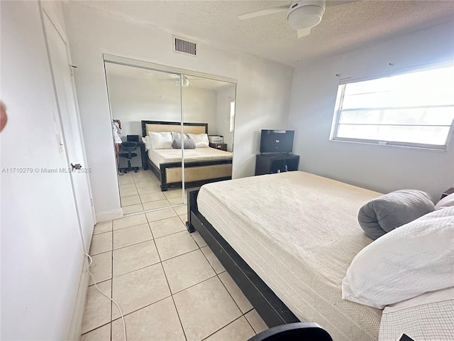 bedroom with ceiling fan, a closet, light tile patterned flooring, and a textured ceiling