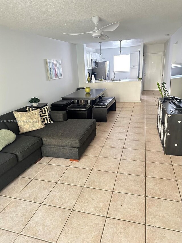 living room with ceiling fan, light tile patterned flooring, and a textured ceiling