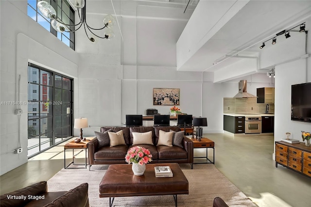 living room featuring plenty of natural light, a towering ceiling, sink, and a chandelier