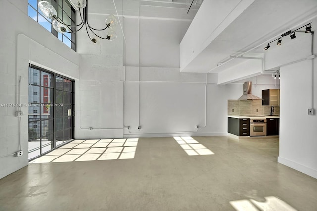 unfurnished living room featuring a towering ceiling, a notable chandelier, and sink