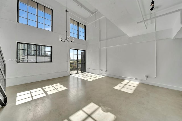 unfurnished living room featuring concrete flooring, a high ceiling, and a notable chandelier