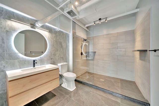 bathroom featuring tiled shower, vanity, tile walls, and toilet