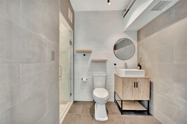 bathroom with toilet, a shower with door, tile patterned floors, and tile walls