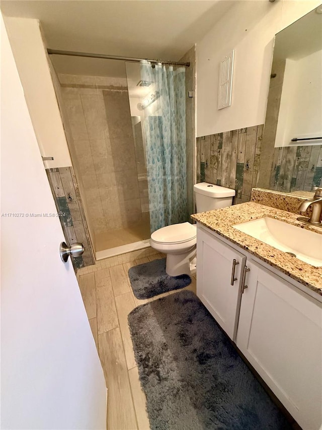 bathroom with curtained shower, vanity, tile walls, and toilet