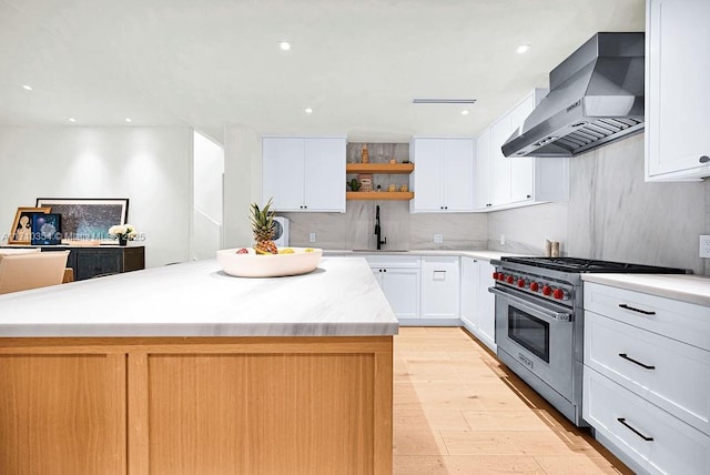 kitchen featuring a center island, sink, wall chimney range hood, designer range, and white cabinets