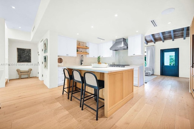 kitchen with white cabinets, light wood-type flooring, a spacious island, and wall chimney range hood