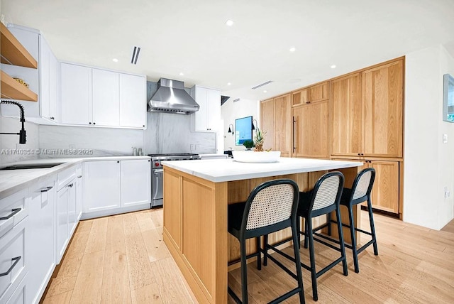 kitchen featuring wall chimney exhaust hood, high end stainless steel range oven, sink, white cabinetry, and a kitchen island