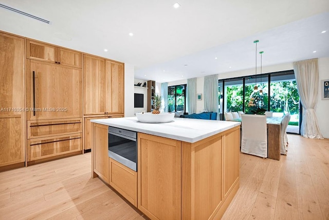 kitchen featuring oven, hanging light fixtures, a kitchen island, and light hardwood / wood-style floors