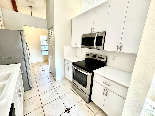 kitchen with white cabinets, a towering ceiling, a textured ceiling, appliances with stainless steel finishes, and light tile patterned flooring