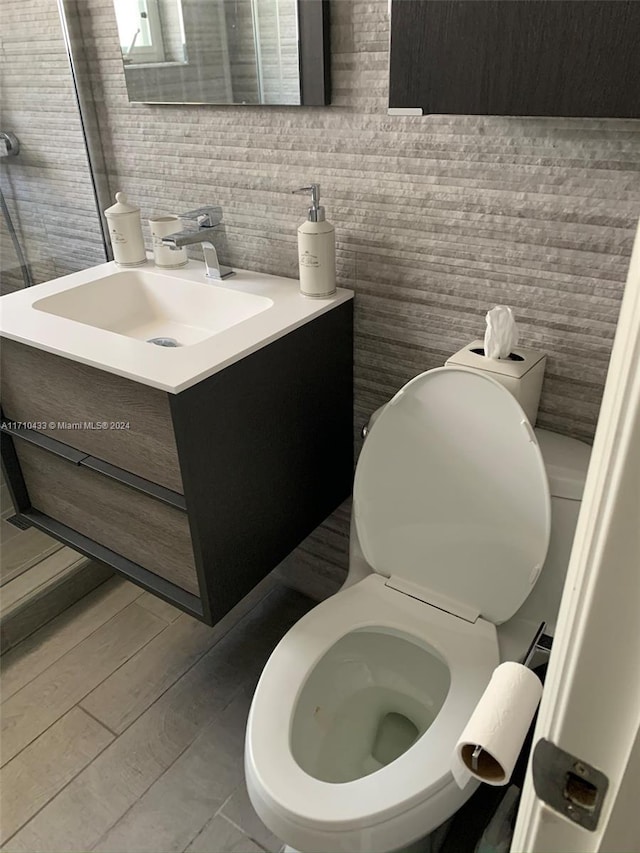 bathroom with vanity, toilet, wood-type flooring, and tile walls