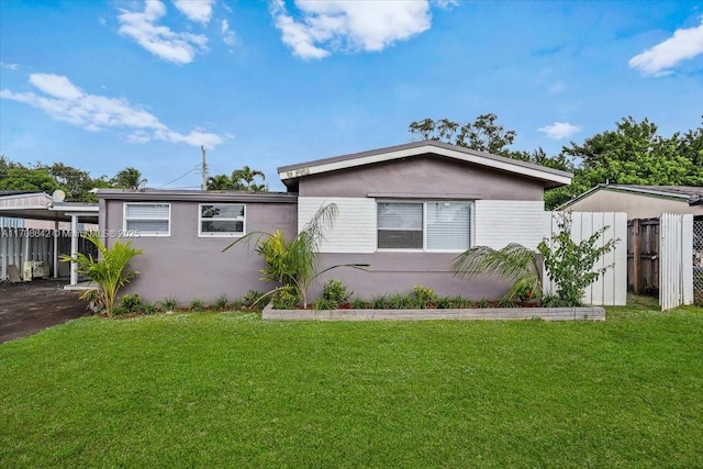 view of front facade featuring stucco siding, fence, a carport, and a front yard