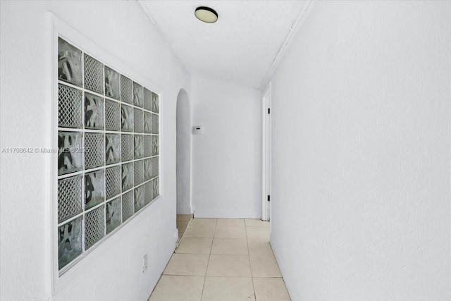 hall with arched walkways and light tile patterned flooring