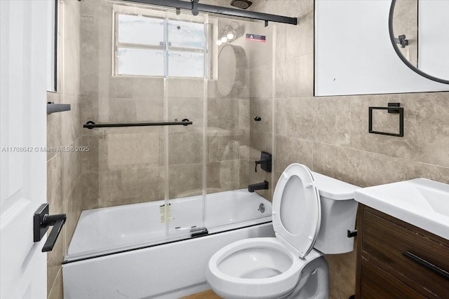 full bathroom with bath / shower combo with glass door, vanity, toilet, and tile walls