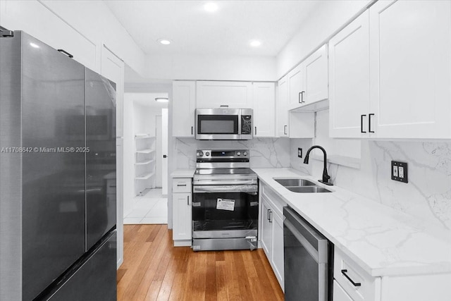 kitchen with light stone counters, stainless steel appliances, a sink, white cabinetry, and light wood-type flooring