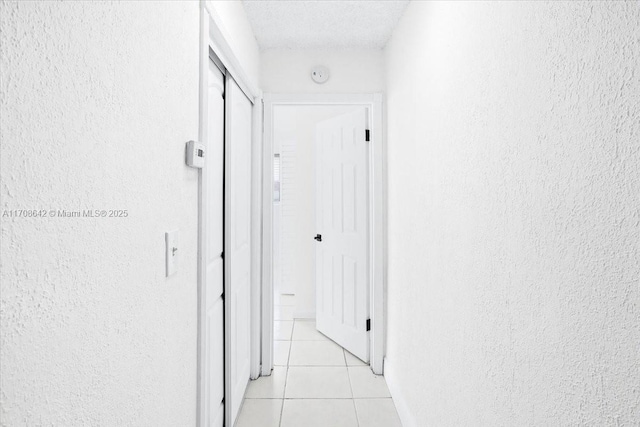 hallway with a textured wall, a textured ceiling, and light tile patterned floors