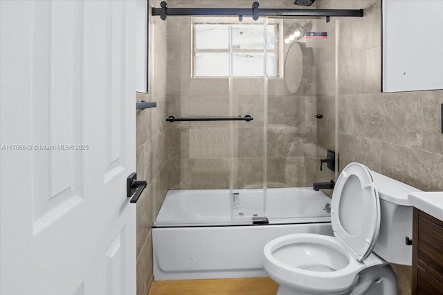 bathroom with combined bath / shower with glass door, vanity, toilet, and tile walls