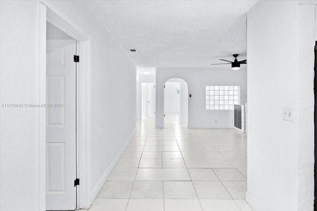 hallway featuring arched walkways, light tile patterned floors, a textured ceiling, and baseboards